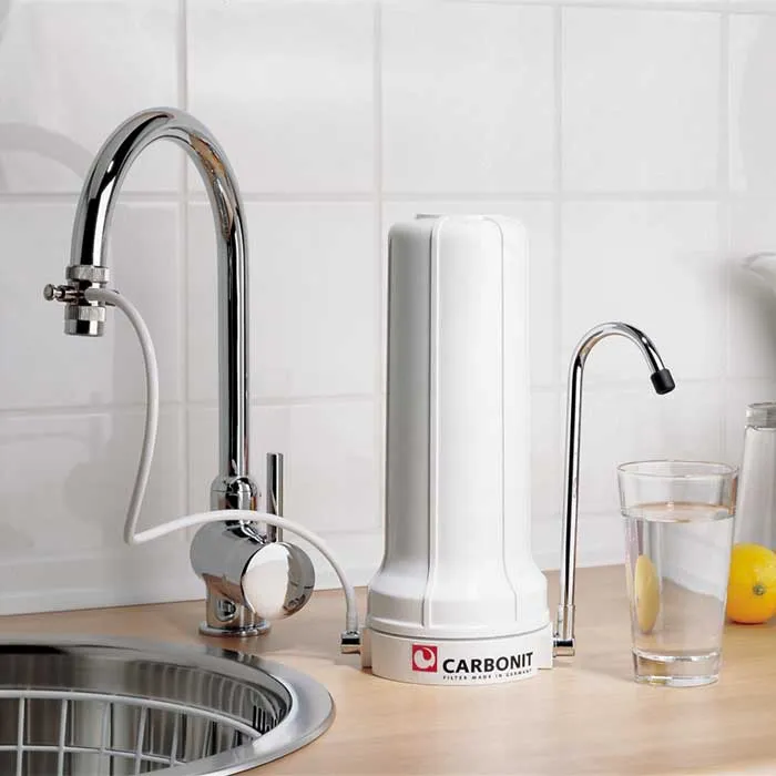 Auftischfilter SanUno 2 Auftischfilter SanUno | Auftischfilter SanUno von Carbonit mit Wasserhahn Ein Auftischfilter für den Anschluss an den regulären Wasserhahn Dazu gratis Glasflasche Lara Das ORIGINAL! Der Carbonit Auftischfilter SanUno ist ein einfacher und hochwertiger Aktivkohlefilter vom Marktführer Carbonit. Ein Auftischfilter zum Anschluss an den regulären Wasserhahn mit CARBONIT® Monoblock NFP Premiumpatronen. Die Carbonit Aktivkohlefilter sind gesinterte d.h. gebackene Aktivkohleblöcke, welche nach einem speziellen Verfahren hergestellt werden. Die daraus entstandenen Aktivkohleblöcke absorbieren Bakterien & Schadstoffe sehr gründlich und geben diese gebundenen Stoffe auch nicht mehr ab. Bei vielen anderen Herstellern besteht das Risiko, dass absorbierte Stoffe wieder herausgespült werden können, wenn die maximale Aufnahmekapazität der Schadstoffe erreicht wurde. Schlussfolgernd trinken Sie dann die Schadstoffe wieder mit. Bei den gesinterten Aktivkohlefiltern von Carbonit ist das nicht der Fall, denn wenn die maximale Aufnahmefähigkeit erreicht ist, leitet die Filterpatrone auch kein Wasser mehr durch. An bereits verminderter Abgabemenge merken Sie, wenn die Aufnahmekapazität langsam erreicht ist. Wählen Sie optional Ihre hochwertigen Filterpatrone(n) zu Ihrem Carbonit SanUno dazu! Wir empfehlen Ihnen entweder die NFP Premium oder die GFP Premium Filterpatrone.